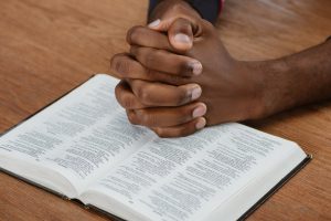 cropped shot of african american man praying with holy bible on wooden table