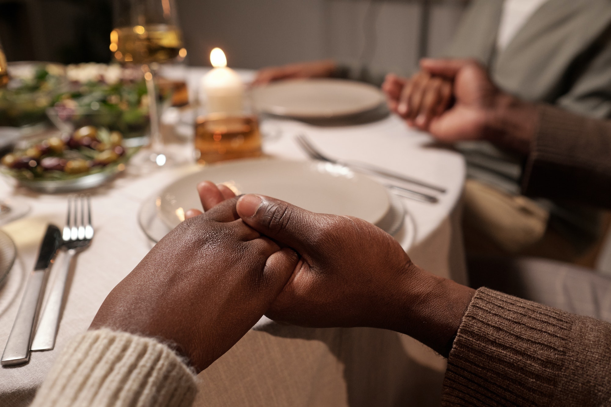 Hands of young African couple during pray by festive table