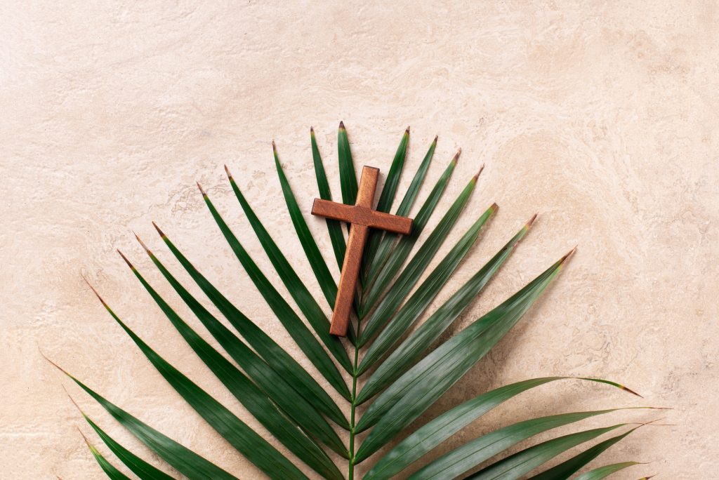 Palm Sunday concept. Wooden cross over palm leaves. Reminder of Jesus sacrifice and Christ